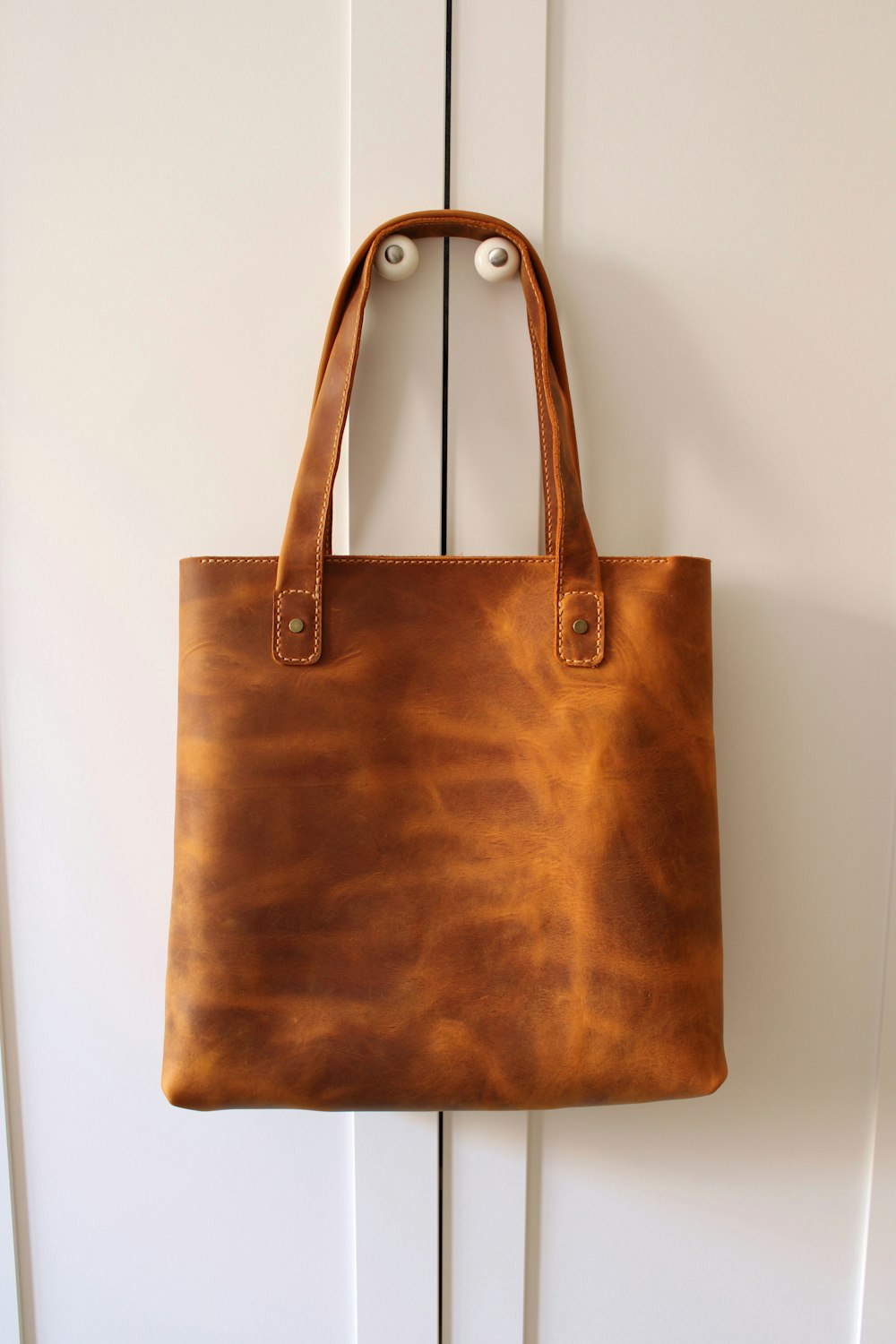 Brown leather tote hanging against a white wall